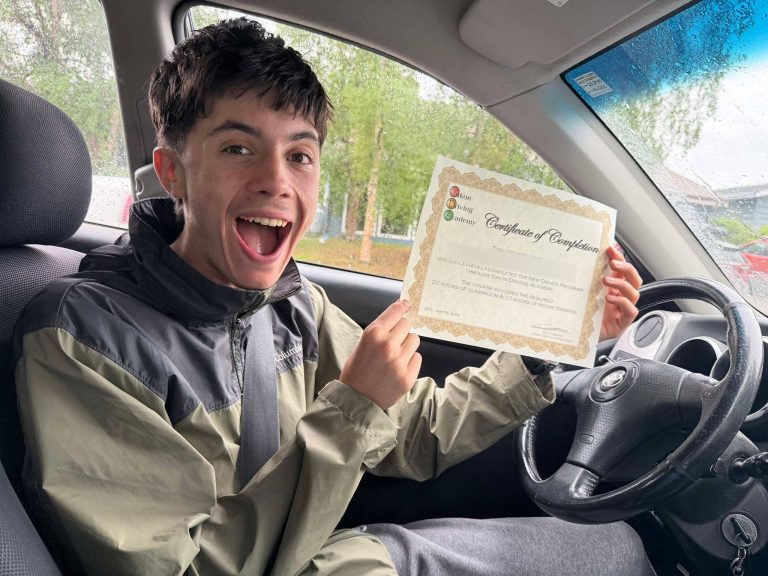 Excited student in the driver's seat holding up his Yukon Driving Academy New Driver Program certificate of completion
